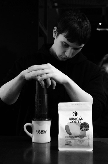 A man brewing with a coffee press beside a Huracán bag